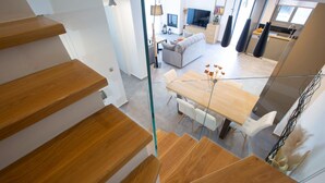 A modern interior with a wooden staircase, a dining area with a wooden table and chairs, and a living space with a sofa and a TV. - Aloft Luxury - Villa Lefkia with heated pool (Apolpena)