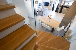 Ein modernes Interieur mit einer Holztreppe, einem Essbereich mit Holztisch und -stühlen sowie einem Wohnbereich mit Sofa und Fernseher.