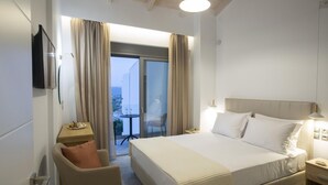 Habitación de hotel con una cama grande, un escritorio, una silla y un balcón con cortinas.