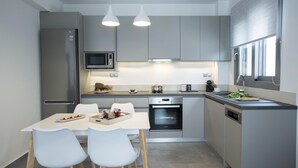 Cocina moderna con gabinetes grises, un refrigerador de acero inoxidable, microondas, horno y lavavajillas. Hay una mesa de comedor con sillas y una ventana que proporciona luz natural.