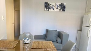 Ein kompakter Wohnbereich mit Esstisch, zwei Stühlen, einer Couch und einem Kühlschrank.