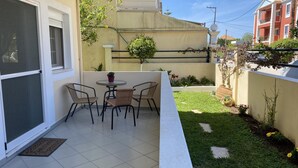 Eine Terrasse mit Tisch und Stühlen, ein kleiner Garten und ein Gebäude im Hintergrund.