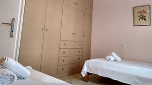 Une chambre à coucher avec une armoire en bois, un lit recouvert d’une courtepointe blanche et une petite table de chevet.