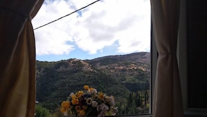 Une pièce avec un lit, une fenêtre avec des rideaux et un vase de fleurs.