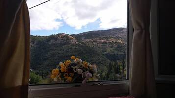 A room with a bed, a window with curtains, and a vase of flowers.