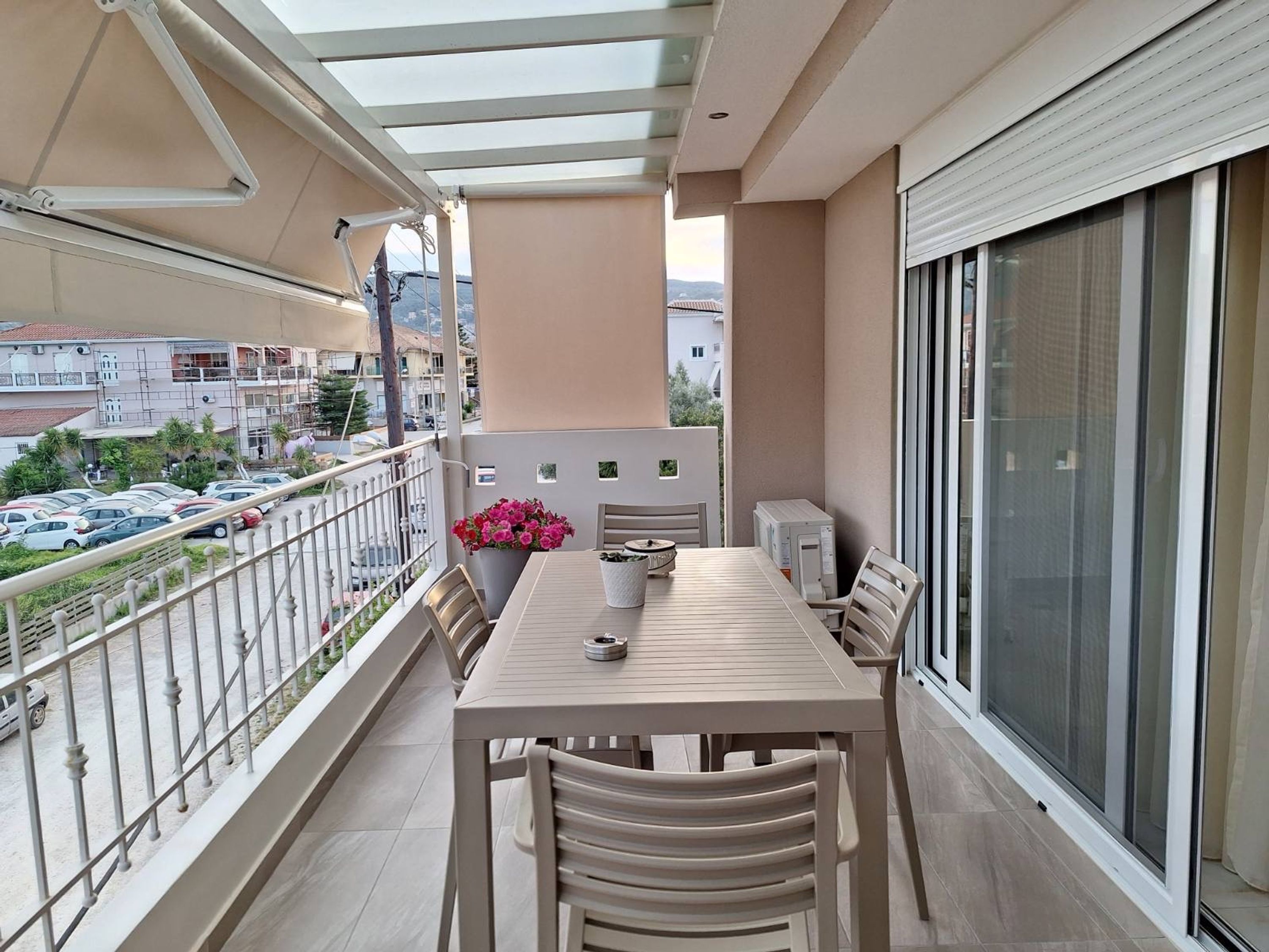 A balcony with a table and chairs, a potted plant, and a view of the street below.