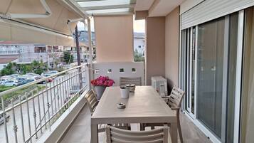 A balcony with a table and chairs, a potted plant, and a view of the street below.