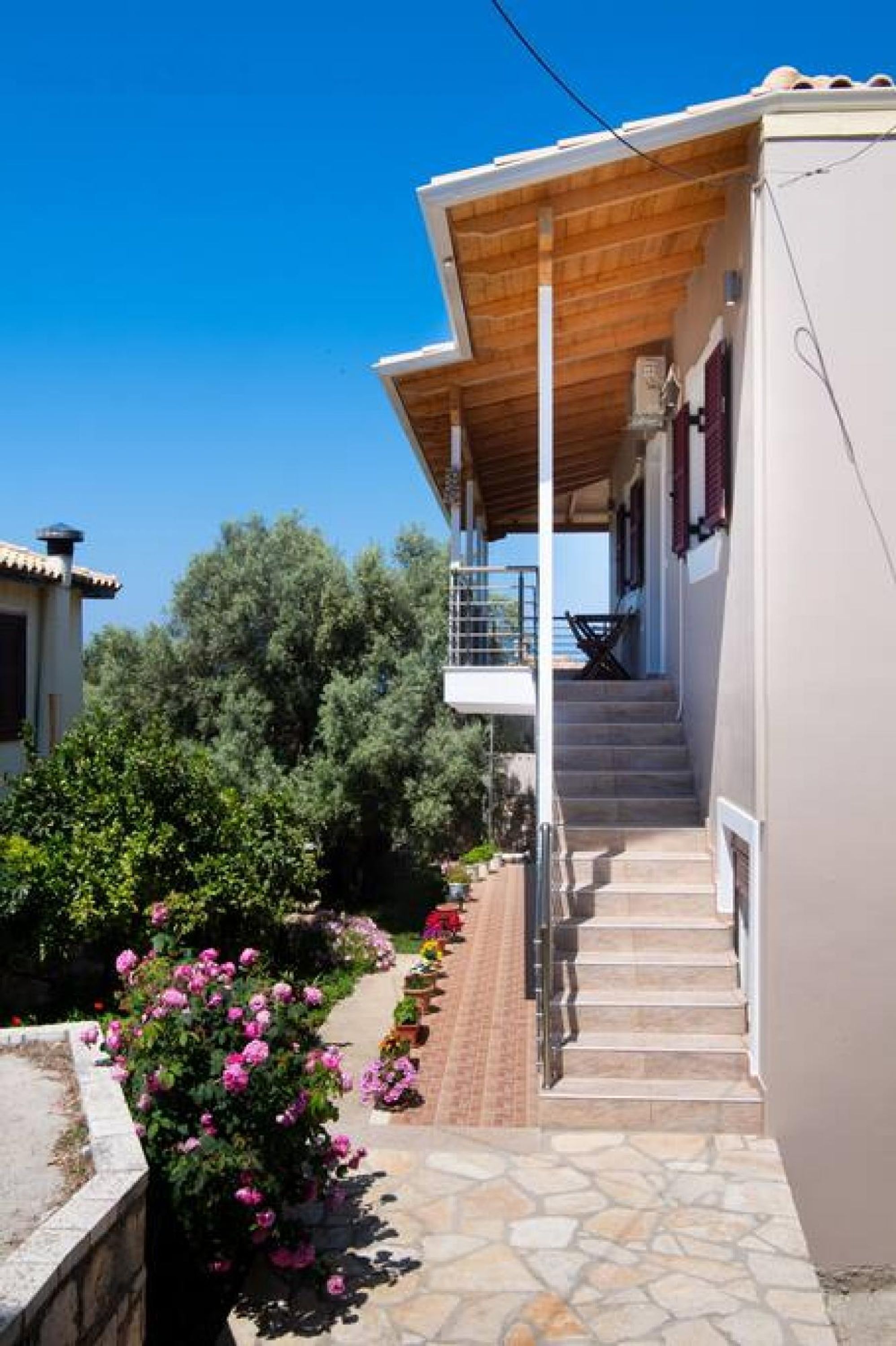 Una casa con porche cubierto, escalones de piedra y un jardín con flores rosadas.