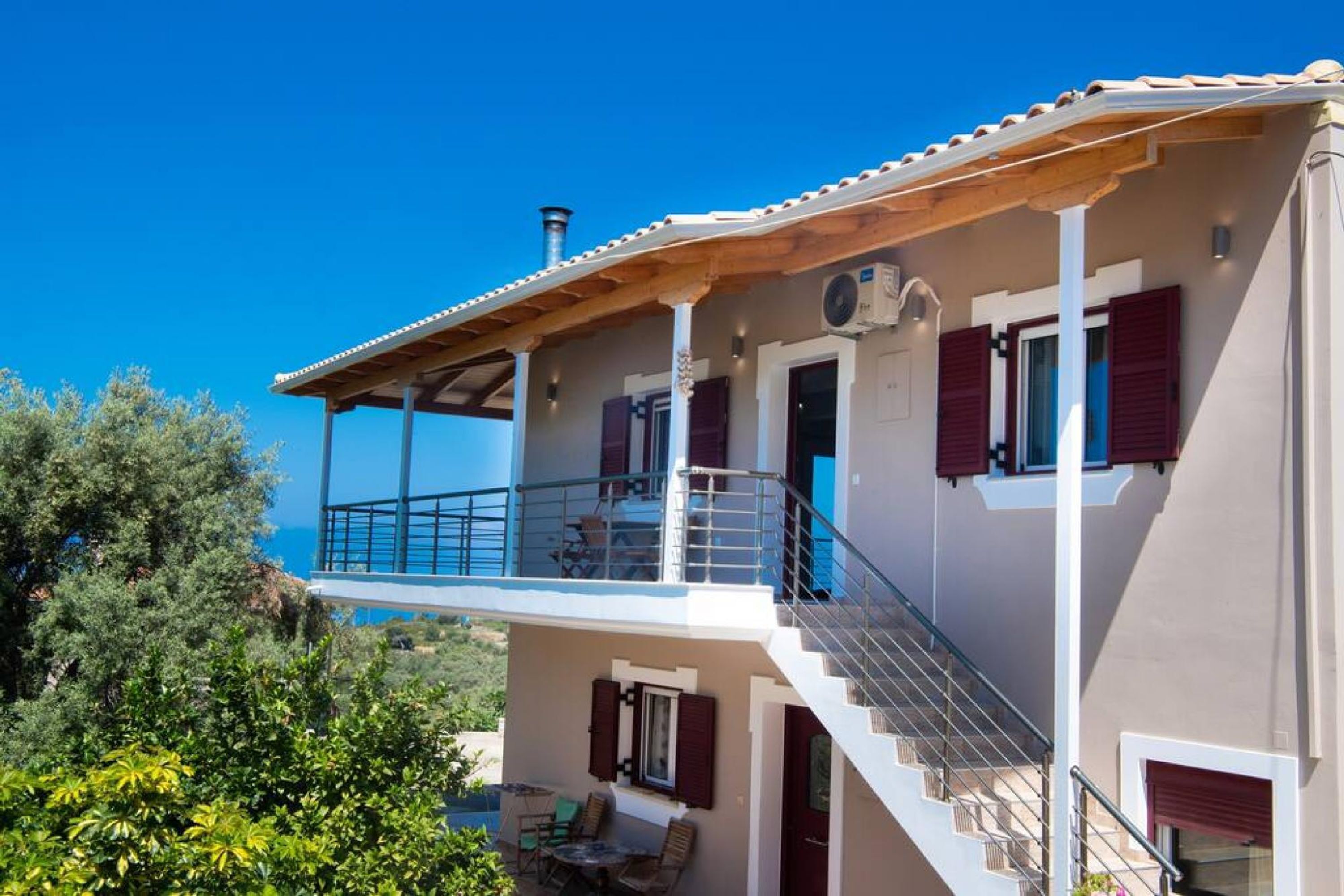 Una casa de dos pisos con balcón, mobiliario exterior y una chimenea.