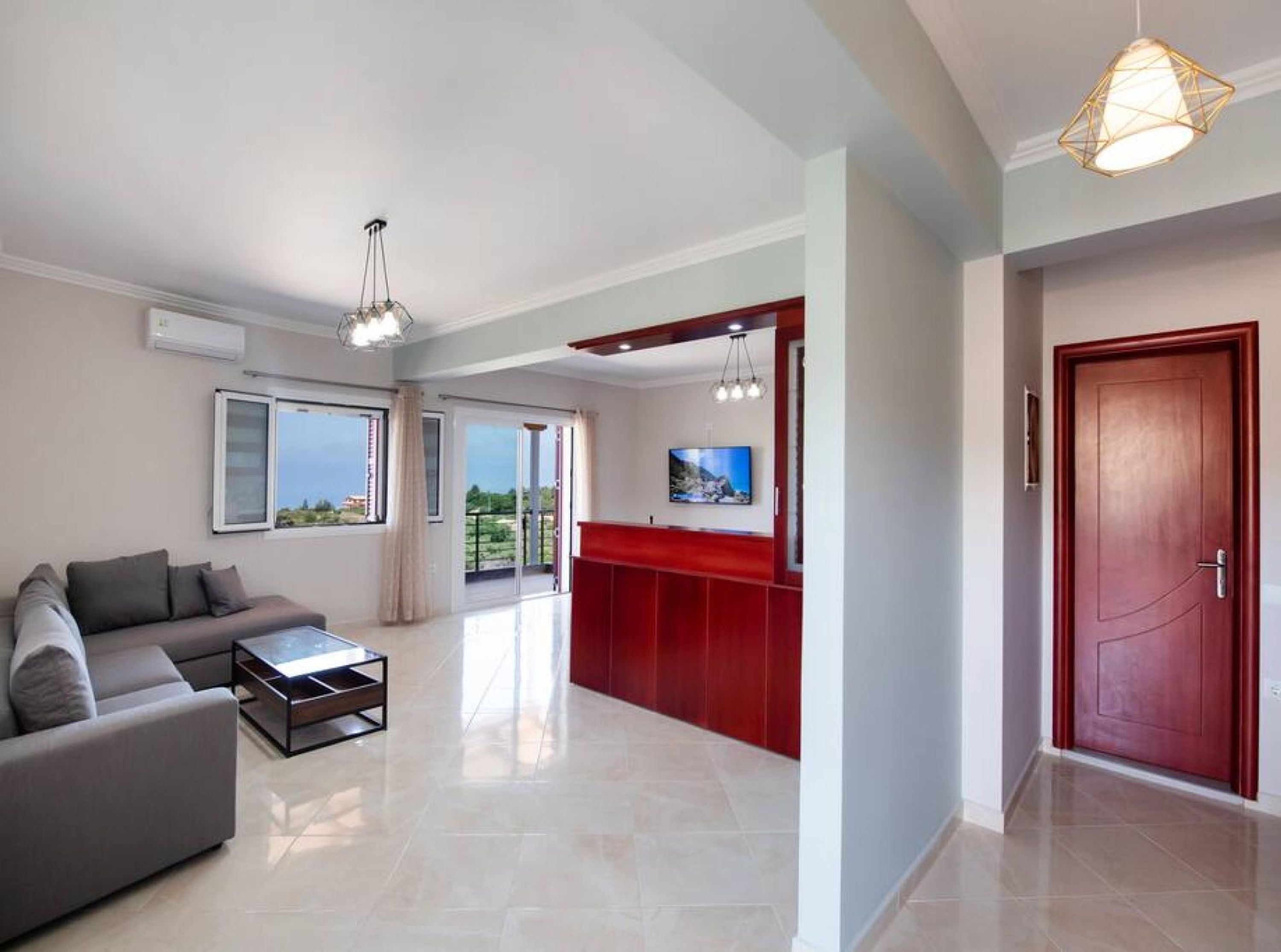 Una sala de estar moderna con un sofá, una mesa de centro y un televisor. Hay una pared de acento roja y una puerta a la derecha.