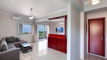 Una sala de estar moderna con un sofá, una mesa de centro y un televisor. Hay una pared de acento roja y una puerta a la derecha.