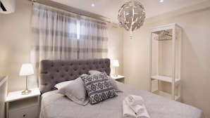 Une chambre à coucher bien rangée, avec une tête de lit capitonnée, deux tables de chevet avec des lampes, un luminaire suspendu en forme de globe, une armoire et une serviette soigneusement pliée sur le lit.