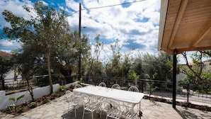 Une terrasse extérieure avec une table et des chaises blanches, entourée d’un sol en pierre et de rampes en métal, sous un ciel dégagé.