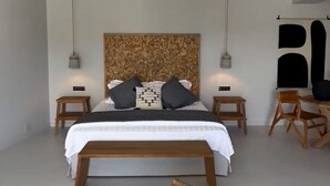 A modern bedroom with a large bed, two bedside tables, a hanging light, a wooden chair, and a large abstract artwork on the wall. - Zephyrus Suite - Cavalier Suites (Nikiana)