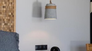 A bedroom with a bed, a bedside table, a lamp, and a wooden wall panel. - Zephyrus Suite - Cavalier Suites (Nikiana)