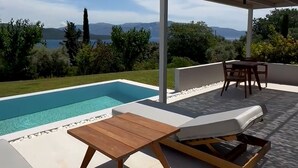 Een zwembadgedeelte met uitzicht op zee, een pergola en buitenmeubilair.