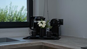 Een keukentafel met een koffiezetapparaat, een kleine vaas met witte bloemen en twee zwarte kopjes.