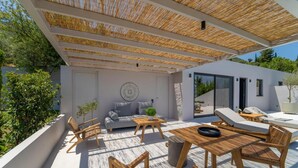 An outdoor patio with a wooden table, chairs, a sofa, and a ceiling with a woven shade. - Duchess Suite - Cavalier Suites (Nikiana)