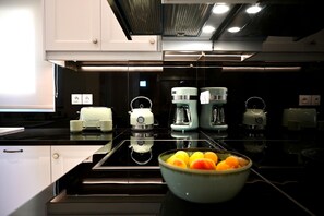 A modern kitchen with a black countertop, white cabinets, and a bowl of fruit. - Villa TheView in Katavolos (Katavolos)
