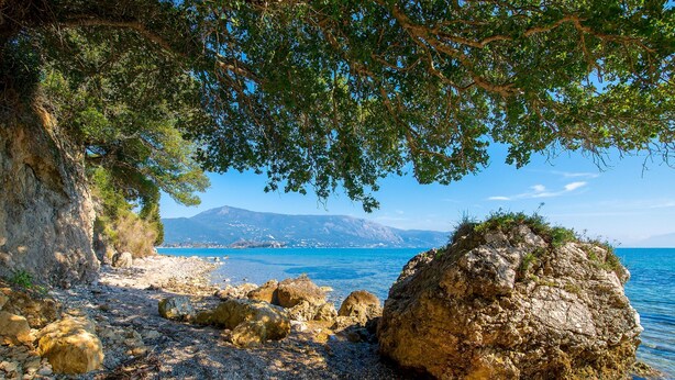 A rocky beach with large boulders and a clear view of the sea and distant mountains. - Villa Spyrelia in Dassia (Dassia)