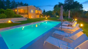 A swimming pool with lounge chairs and umbrellas, surrounded by a landscaped garden and a house with a balcony. - Villa Spyrelia in Dassia (Dassia)