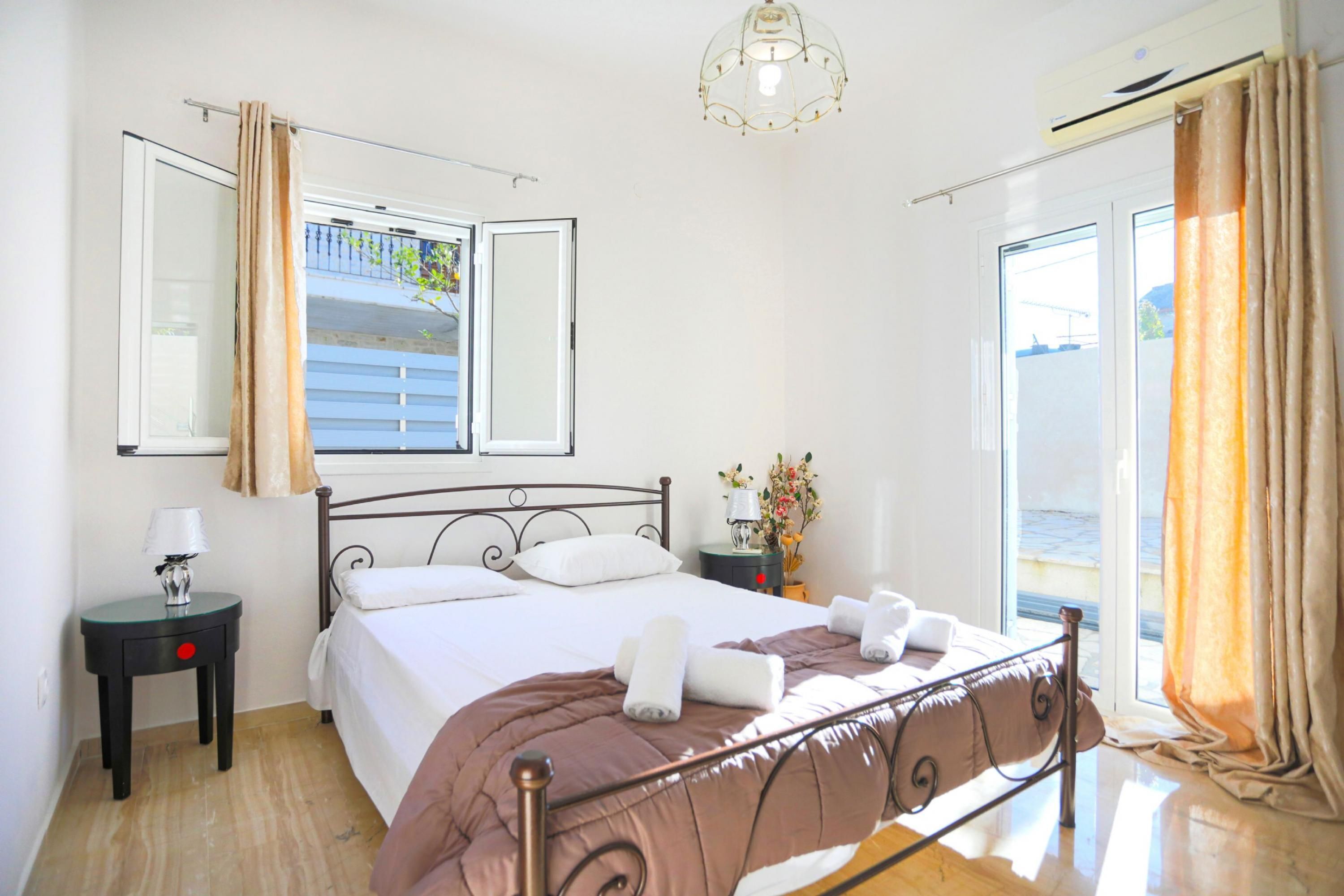A bedroom with a bed, a nightstand, a lamp, a window with curtains, and a view of the sea.