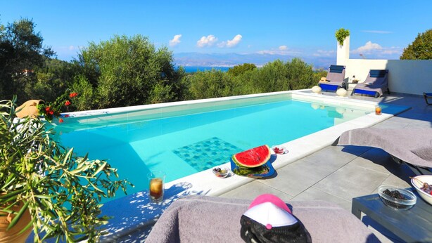 Ein Poolbereich mit Liegestühlen, einer Wassermelone und Blick auf das Meer.