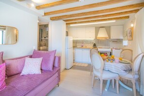 A modern kitchen with white cabinets, a dining table with chairs, and a pink sofa with patterned cushions. - Casa Trenta Otto-J in Corfu (Corfu)