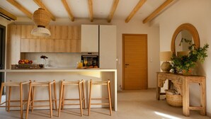 Een moderne keuken met houten kastjes, een centraal eiland met krukken, een hanglamp en een houten deur.