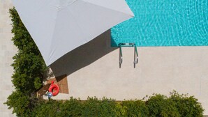 Luchtbeeld van een zwembad met een witte parasol, een reddingsboei en een trap.