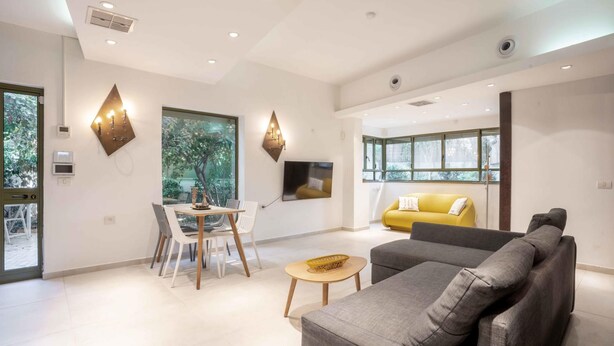 A modern living room with a grey sofa, a yellow armchair, and a dining area with a table and chairs. - Ben Yehouda Jonquille (Tel Aviv-Yafo)