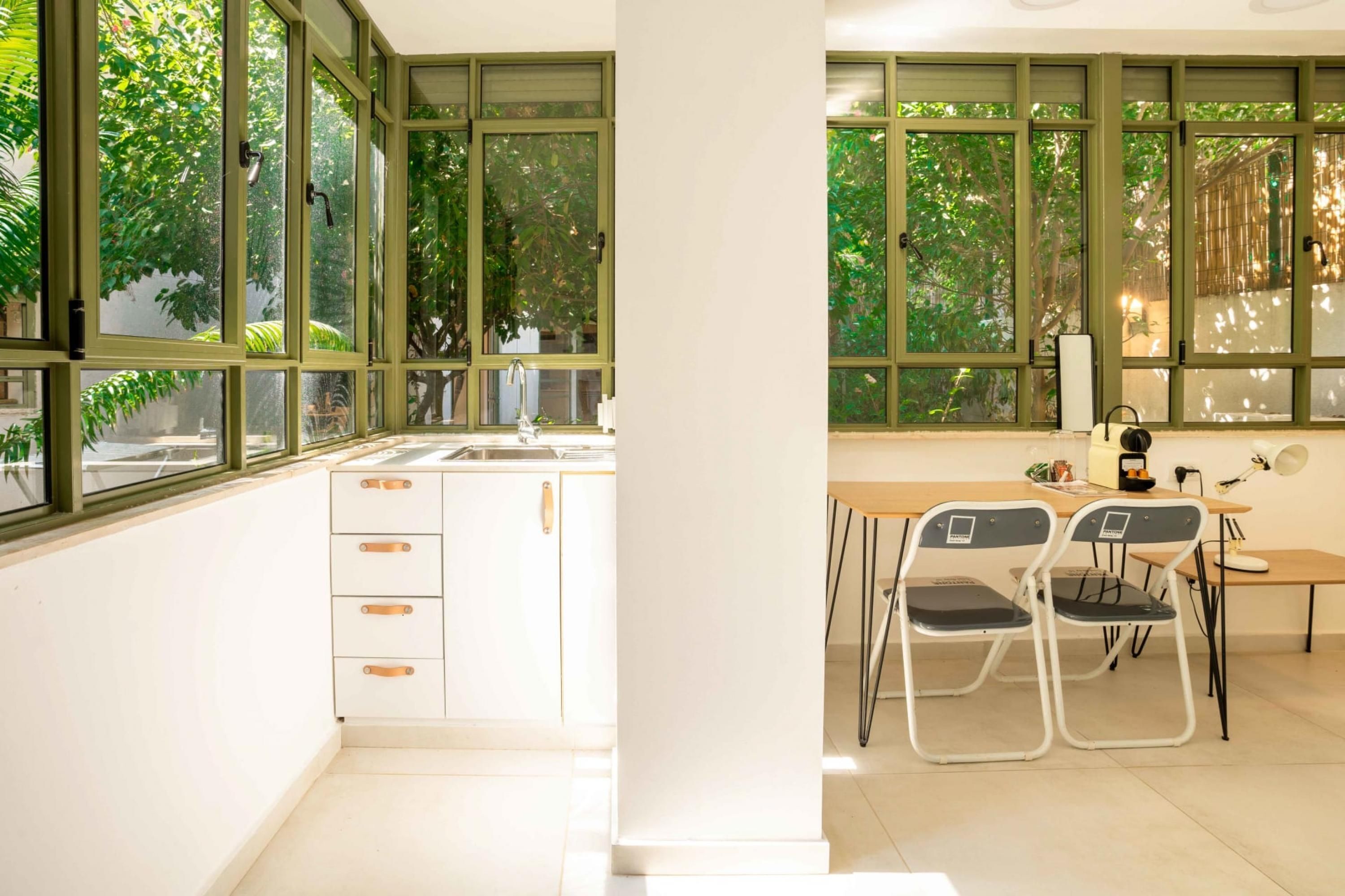 A modern kitchen with a sink, cabinets, and a dining area with chairs and a table.