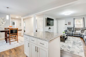 Eine moderne Küche mit weißen Schränken, einer Arbeitsplatte aus Granit und einem Essbereich mit Holztisch und -stühlen.