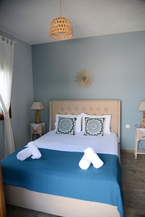 Ein ordentlich bezogenes Bett mit blauer Bettdecke und dekorativen Kissen, eine hängende Leuchte und eine Wanddekoration in Form einer Sonne.