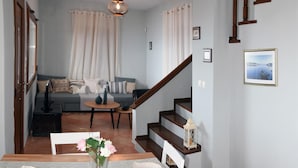 Et spiseområde med et træbord og stole, en vase med blomster, en trappe, en sofa og billeder i rammer på væggen.