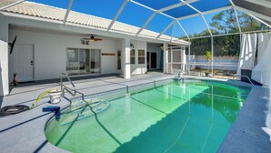 Piscina coberta com céu azul límpido acima, um edifício branco com telhado telhado e uma pequena área de jardim visível pelo teto transparente.
