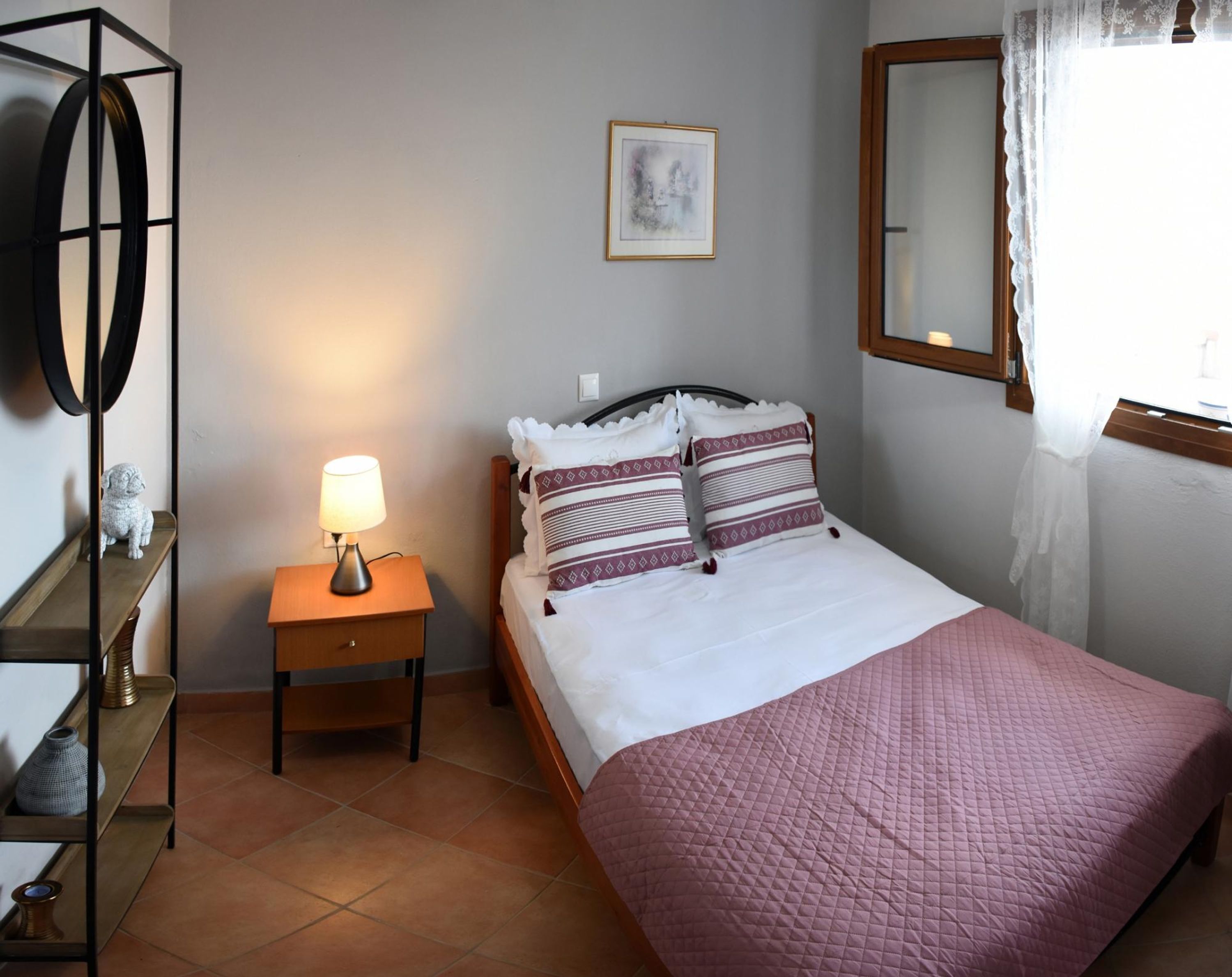 Ein ordentlich eingerichtetes Schlafzimmer mit einem Bett, einer Nachttischlampe, einem Spiegel und einem gerahmten Bild an der Wand.
