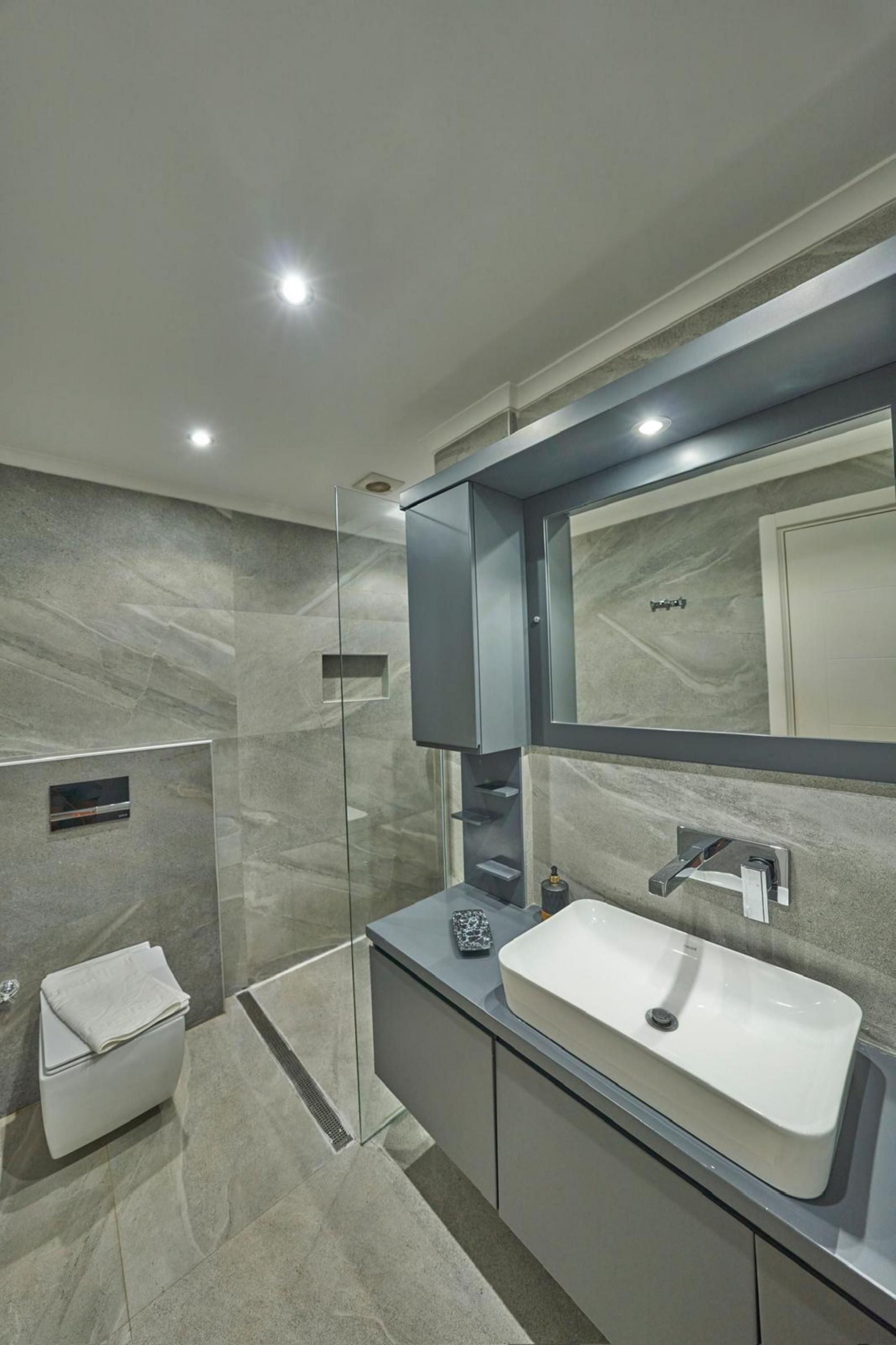 A modern bathroom with a glass shower enclosure, a white sink, and a large mirror.