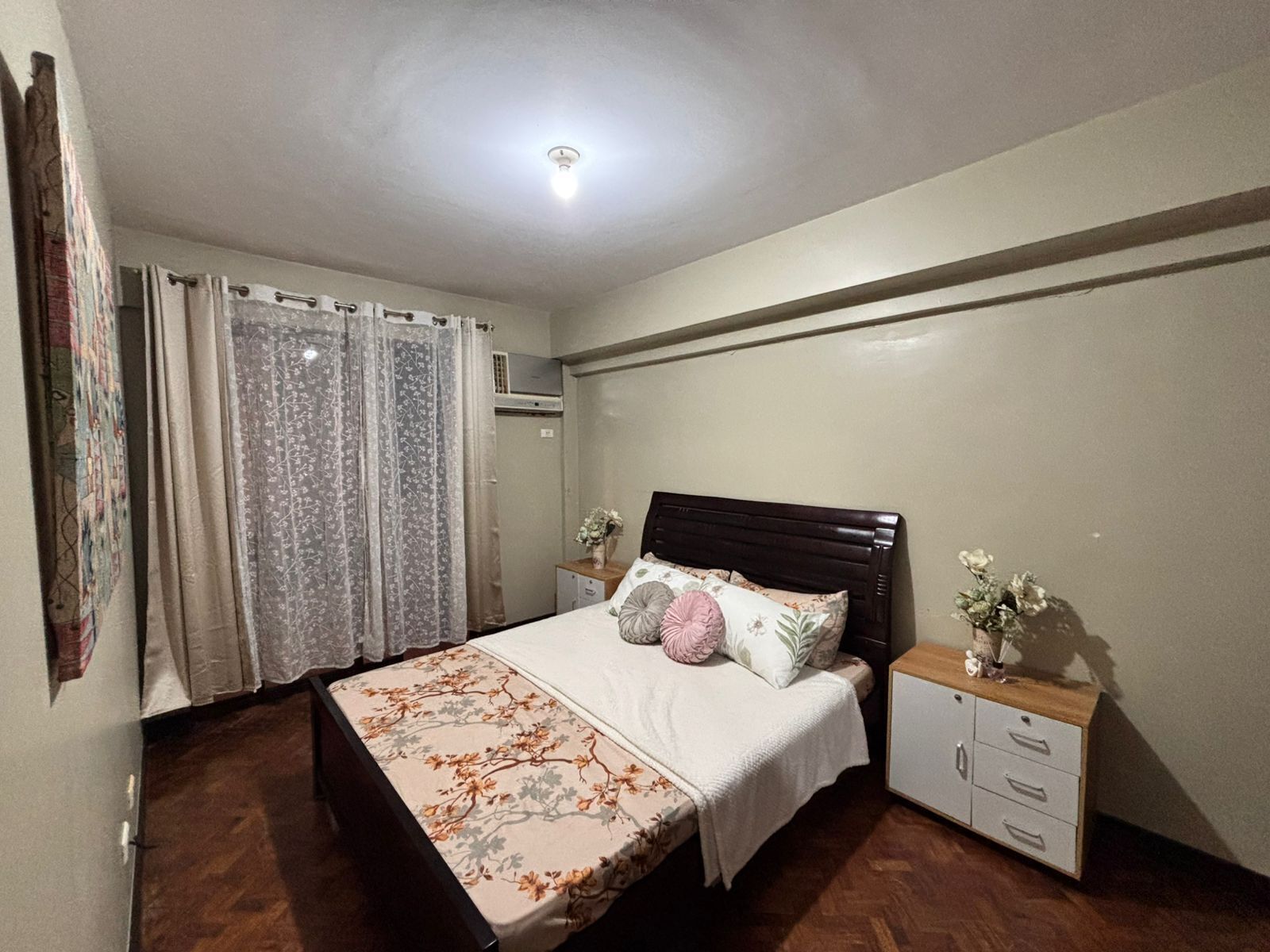 A bedroom with a bed, a nightstand, a dresser, and a window with curtains.