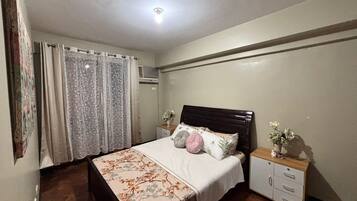 A bedroom with a bed, a nightstand, a dresser, and a window with curtains.