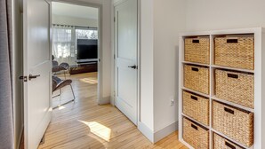 Un pasillo con una puerta blanca que da a una habitación con televisión y sofá. Se ven cestos de mimbre en estantes a la derecha.