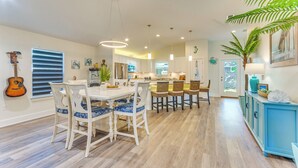 Una cocina moderna con armarios blancos, un comedor con sillas blancas y un mueble azul.