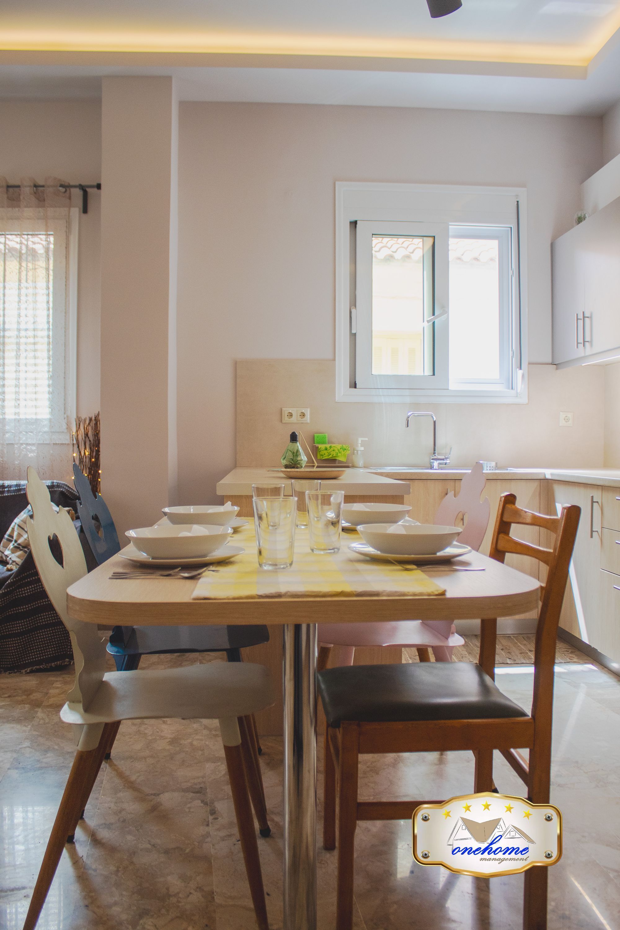 Un coin repas avec une table dressée pour quatre personnes, une fenêtre au-dessus de l’évier et une vue sur l’extérieur.