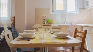 Un coin repas avec une table dressée pour quatre personnes, une fenêtre au-dessus de l’évier et une vue sur l’extérieur.