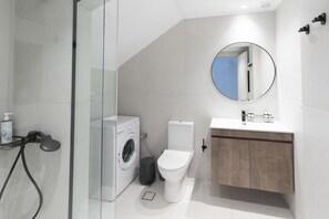 Ein modernes Badezimmer mit Duschkabine aus Glas, einer Waschmaschine, einer Toilette und einem Badezimmer-Waschtisch aus Holz mit Spiegel.