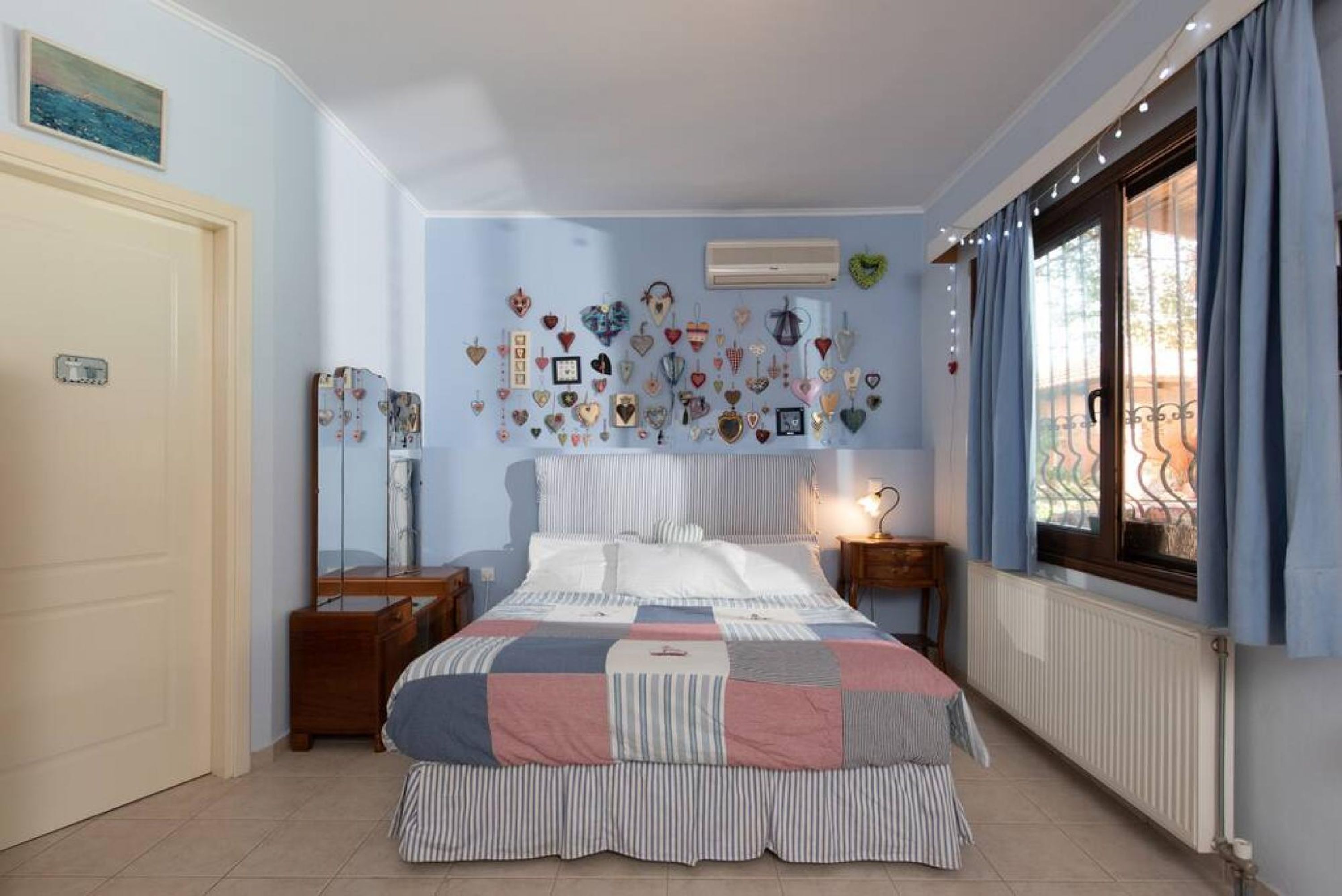 Ein Schlafzimmer mit Bett, Nachttisch, Wand mit herzförmigen Dekorationen und Fenster mit Vorhängen.