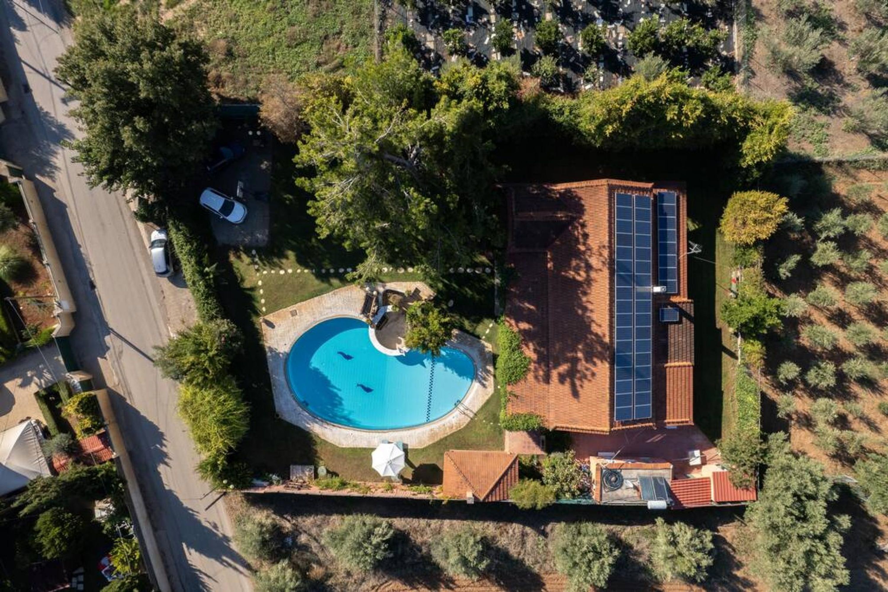 Vue aérienne d’une propriété résidentielle dotée d’une piscine, d’une maison en briques et d’un ensemble de panneaux solaires.