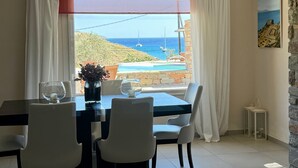 Ein Essbereich mit Tisch, Stühlen und Meerblick durch große Fenster.