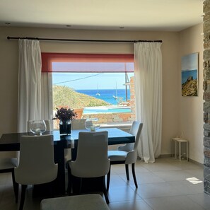 Ein Essbereich mit Tisch, Stühlen und Meerblick durch große Fenster.