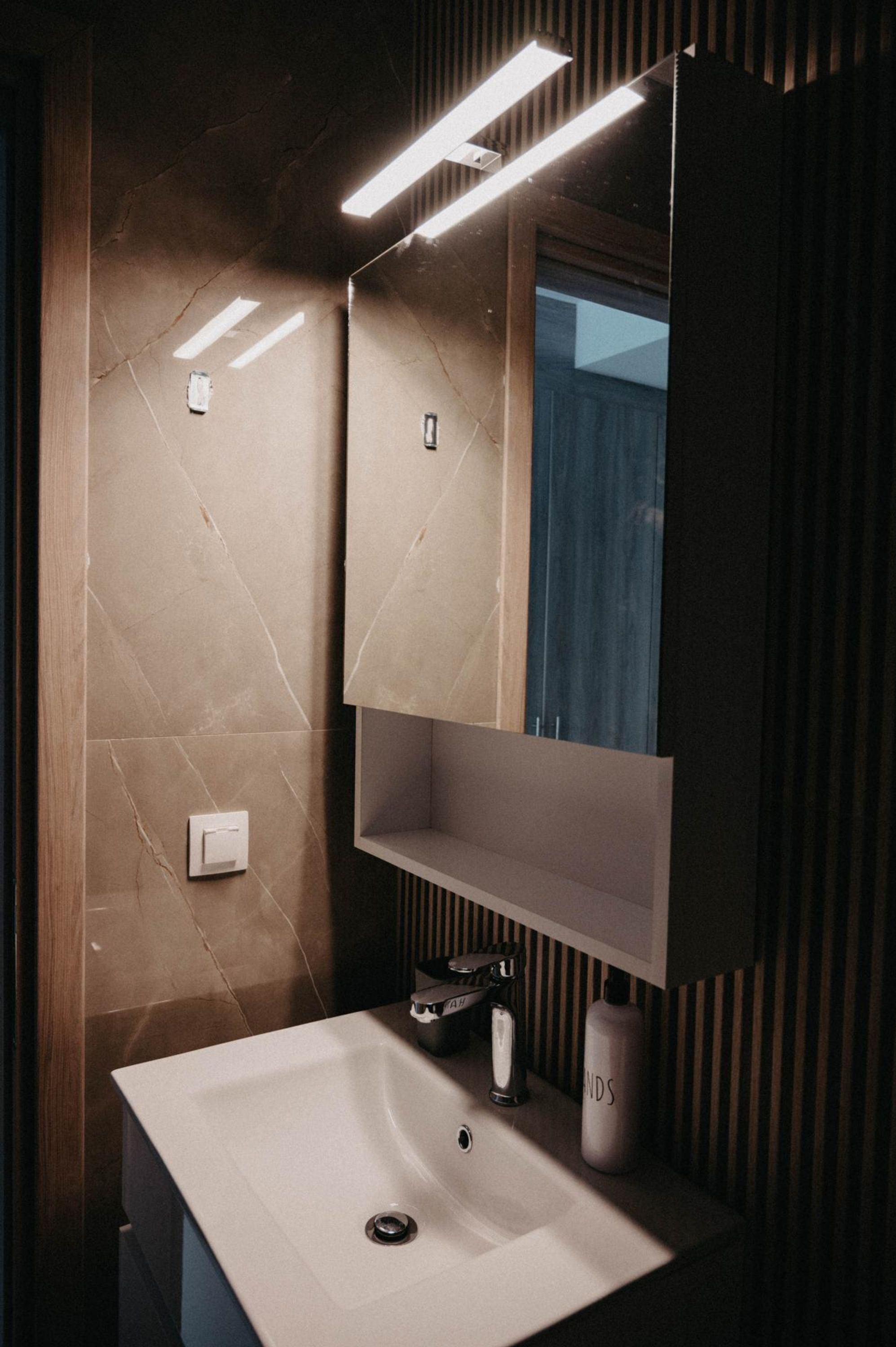A modern bathroom with a white sink, a mirror, and a light fixture above the mirror.